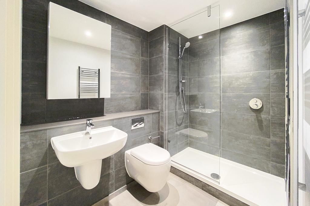 Modern bathroom with gray tiled walls, white sink and toilet, glass shower.