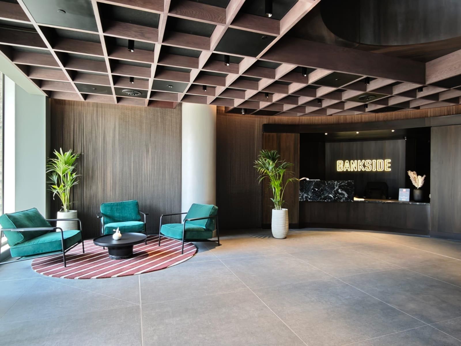 Lobby with teal chairs, plants, patterned rug, and a reception desk with