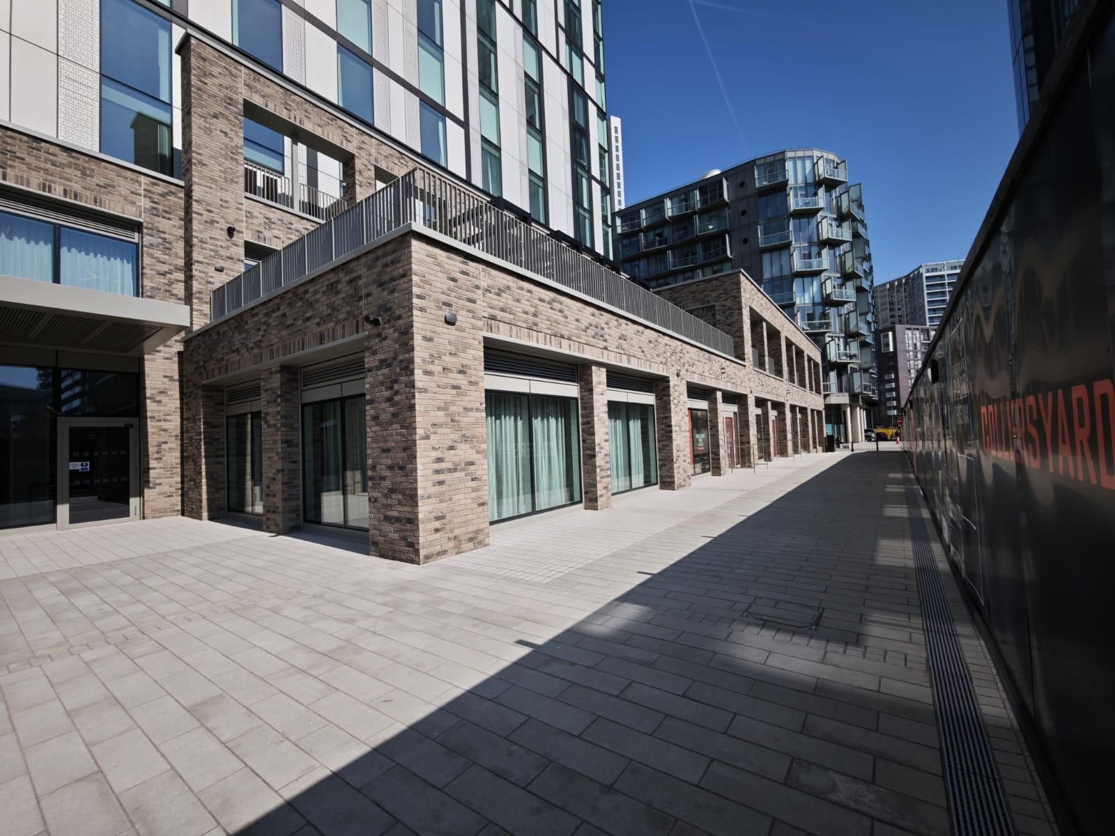Brick building with windows and a rooftop patio. Paved walkway with shadows on a sunny day.