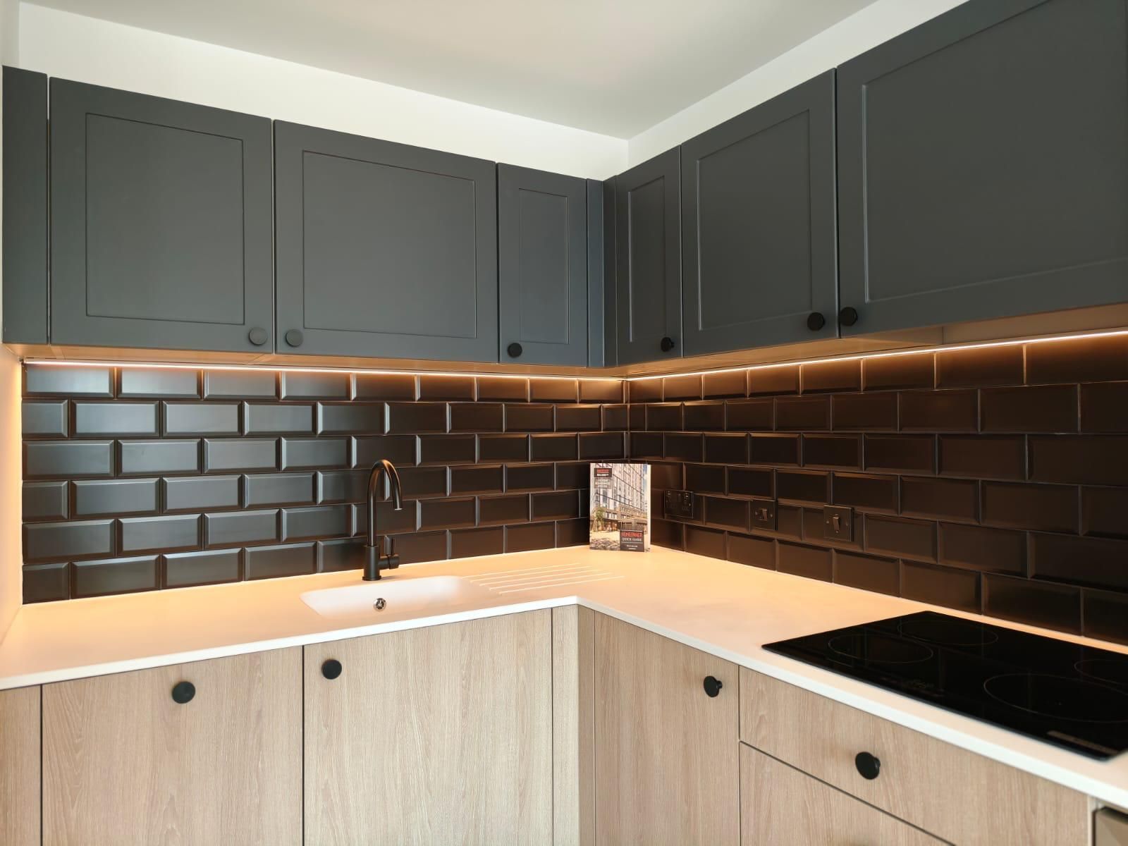 Modern kitchen corner with gray upper cabinets, black subway tile backsplash, and light wood lower cabinets.