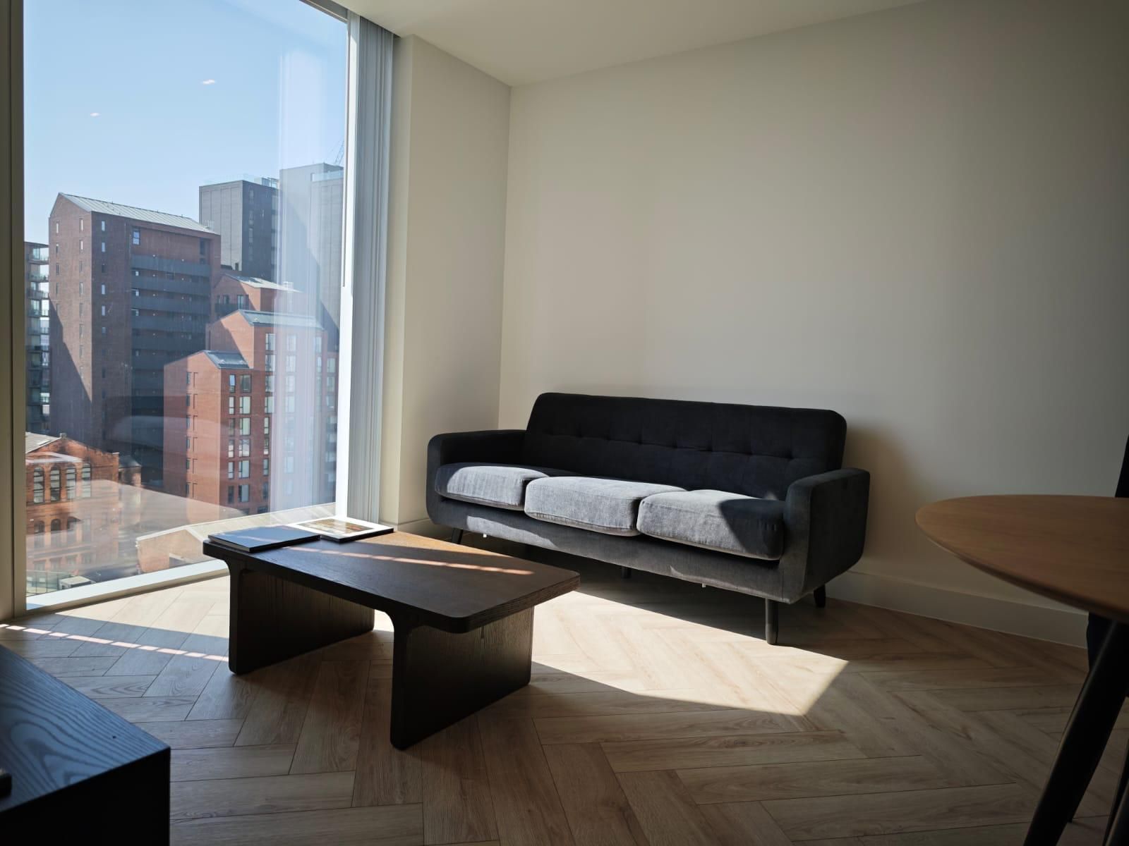 Living room with city view: dark gray sofa, wood coffee table, large window, wood floor.
