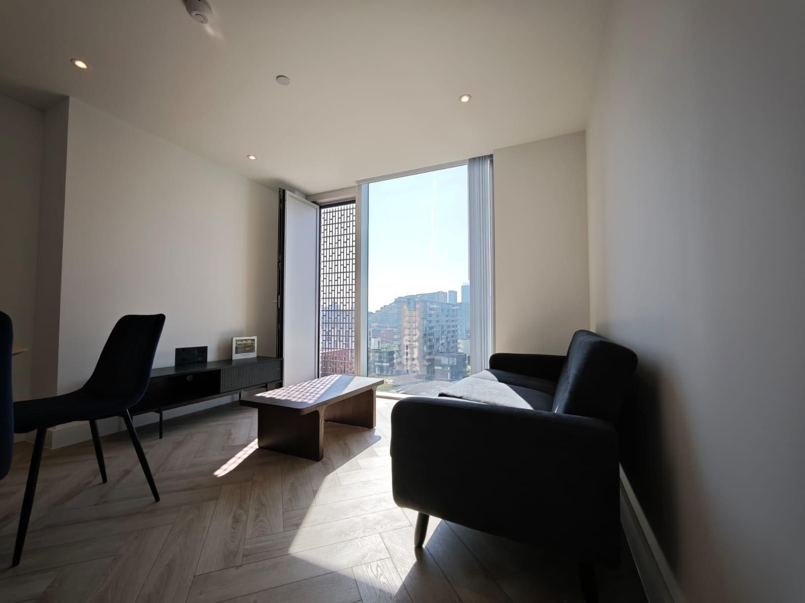 Modern living room with black sofa, table, and tall window overlooking city buildings.