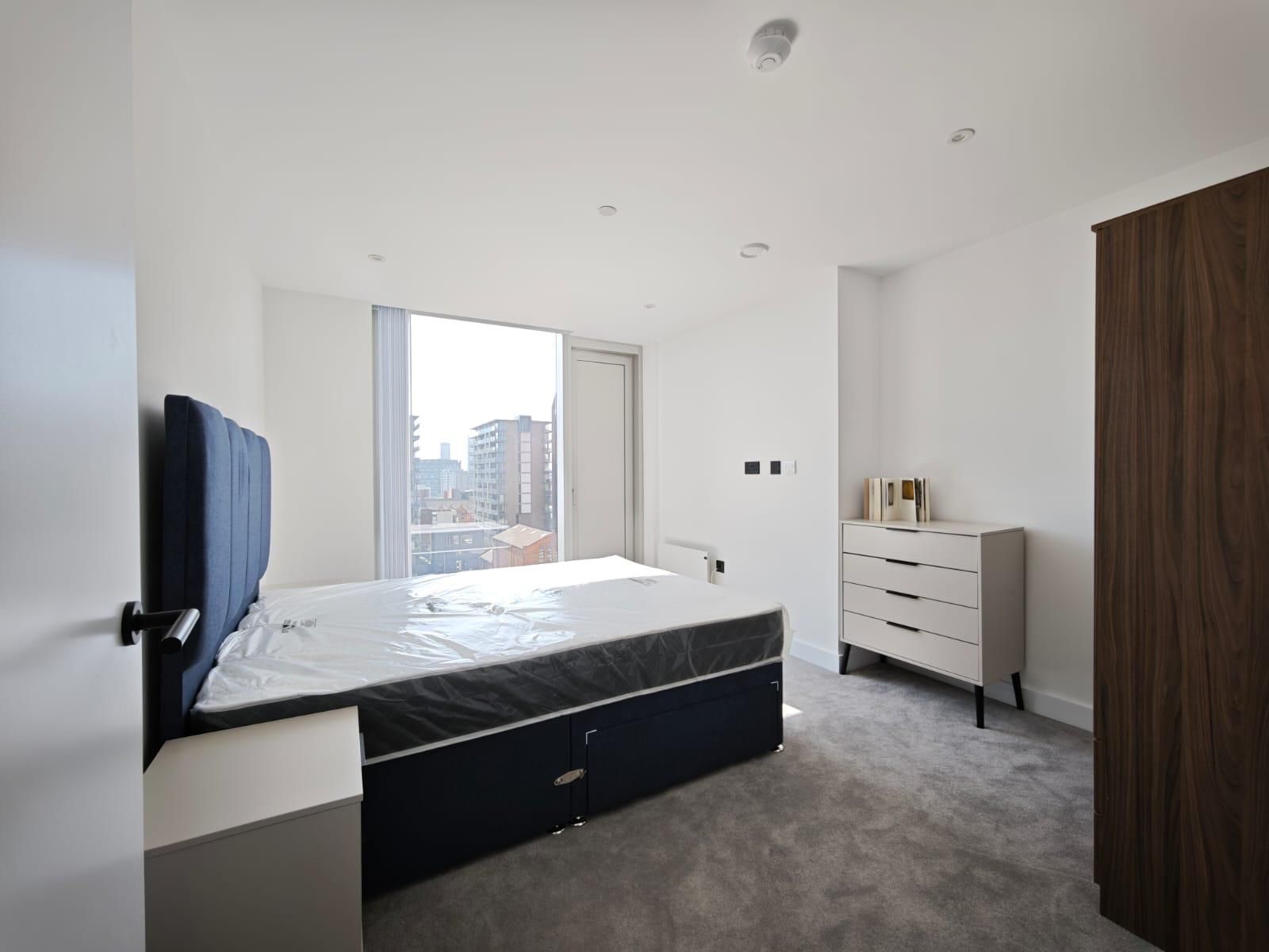 Bedroom with a large bed, window, dresser, and wardrobe; light gray carpet and white walls.