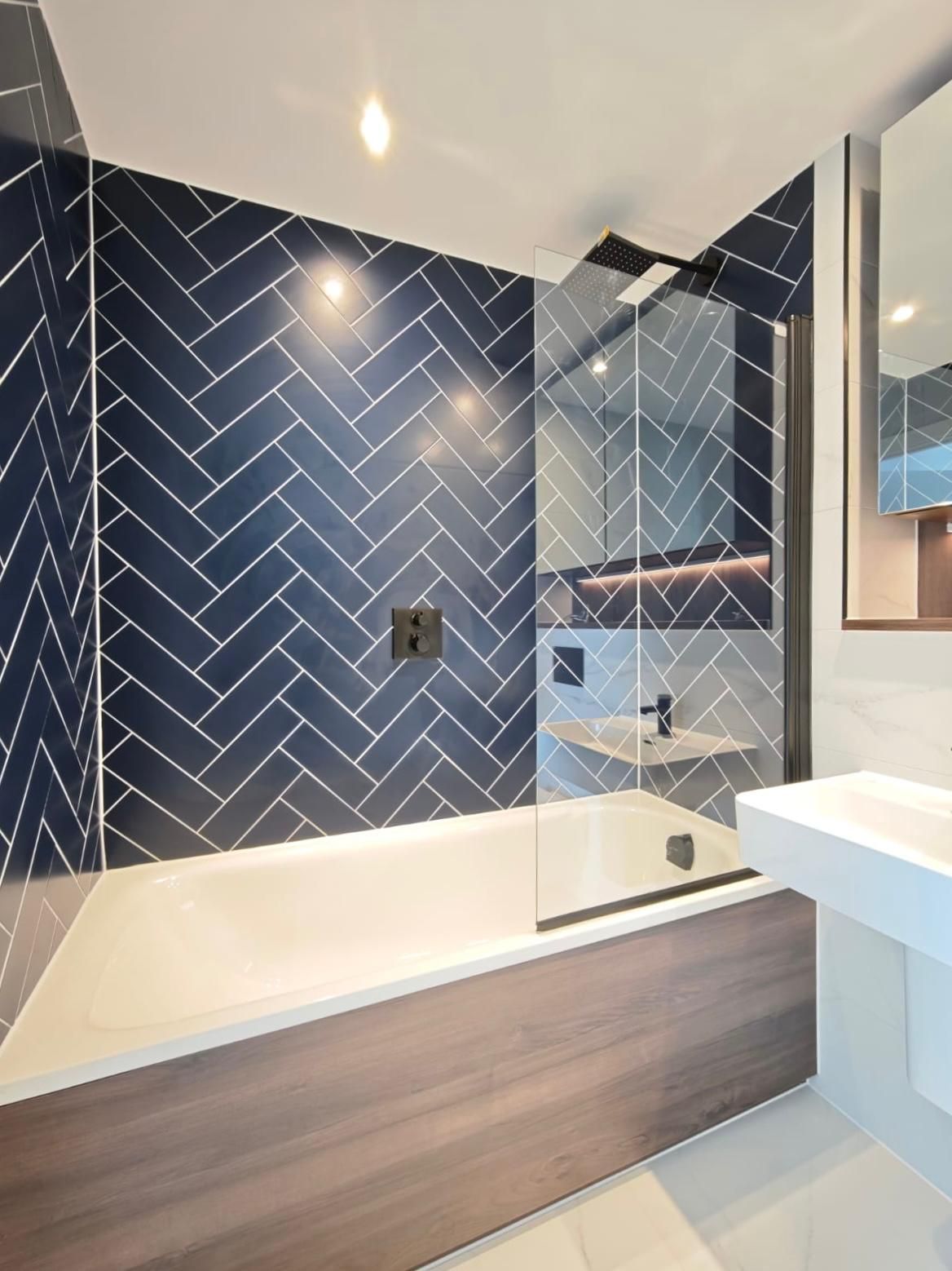 Modern bathroom with dark blue herringbone tile, glass shower door, and wood-look flooring.