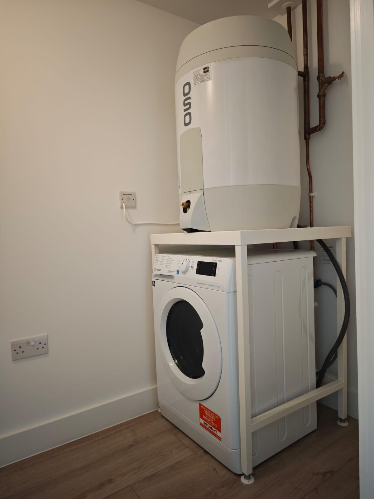 Washing machine with a water heater on top, in a white-walled laundry area.
