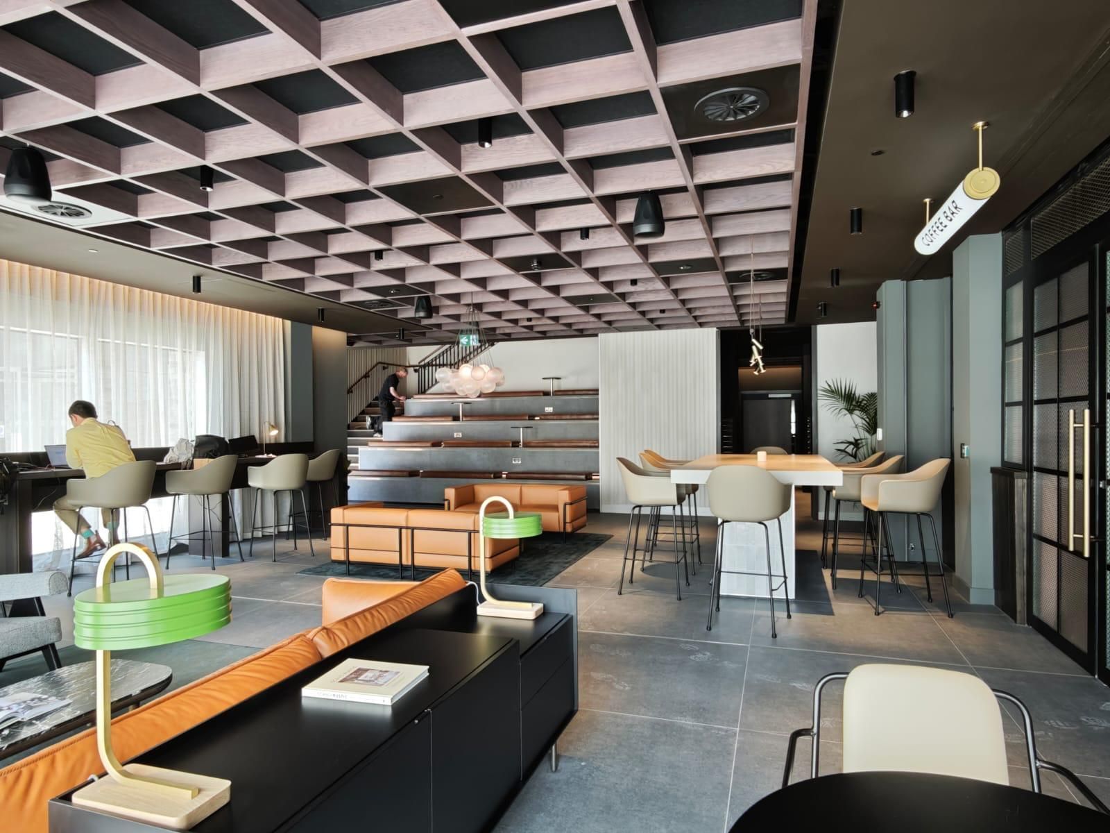Modern hotel lobby with grid ceiling, seating areas, and a staircase.
