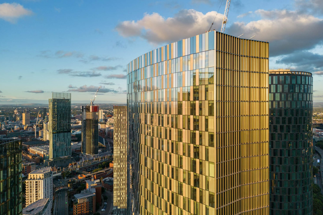 Modern high-rise buildings in Manchester, England, with golden and reflective glass facades.