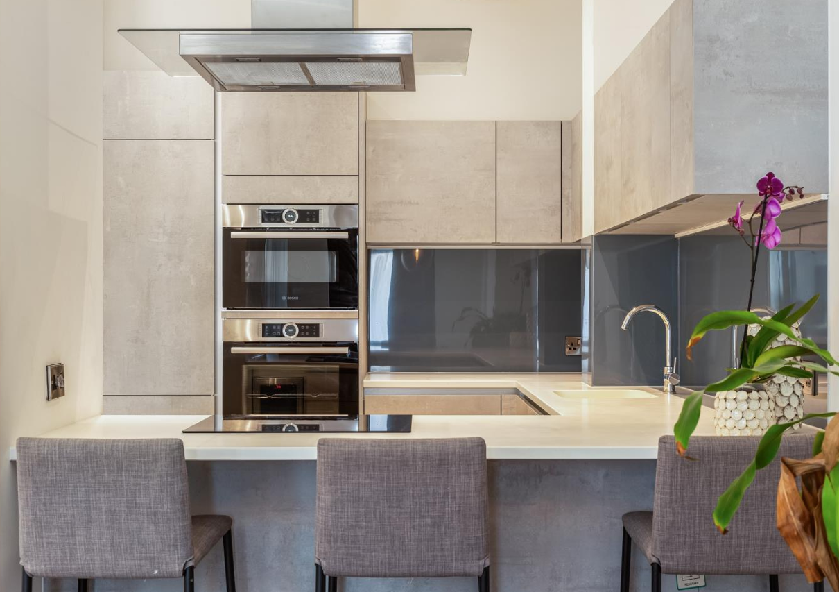 Modern kitchen with light grey cabinets, stainless steel appliances, and bar seating.