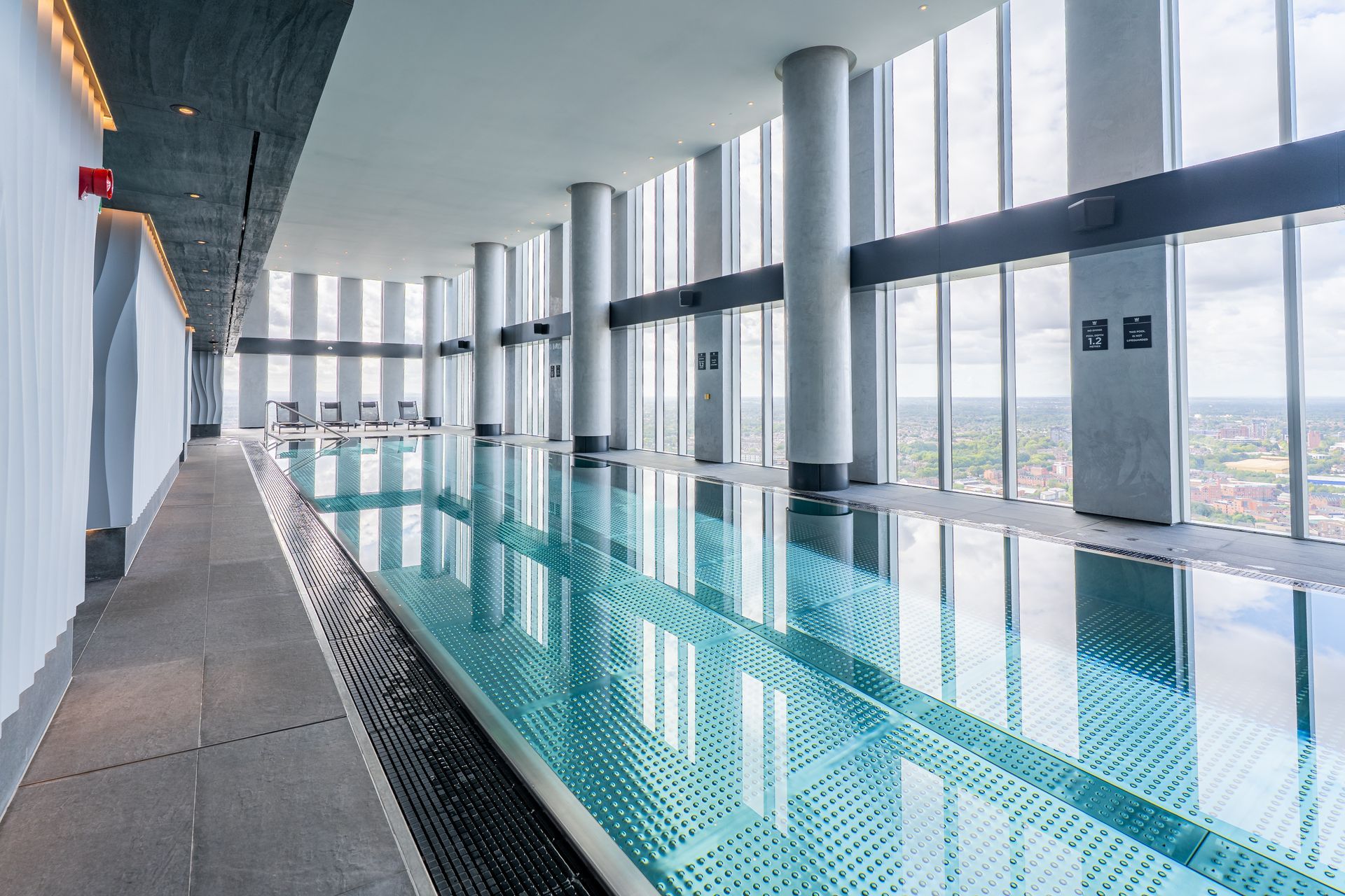 Indoor swimming pool, tall windows, cityscape view, concrete pillars, calm water.