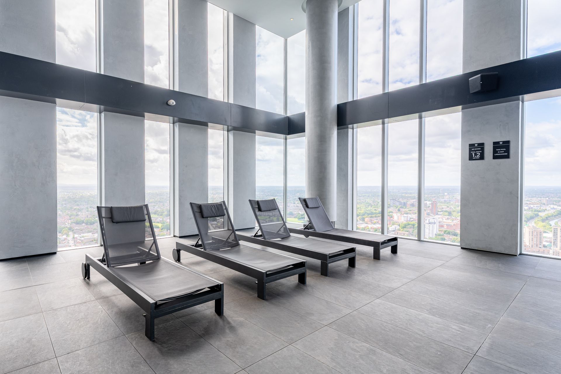 Four gray lounge chairs in a room with large windows, looking out over a cityscape.