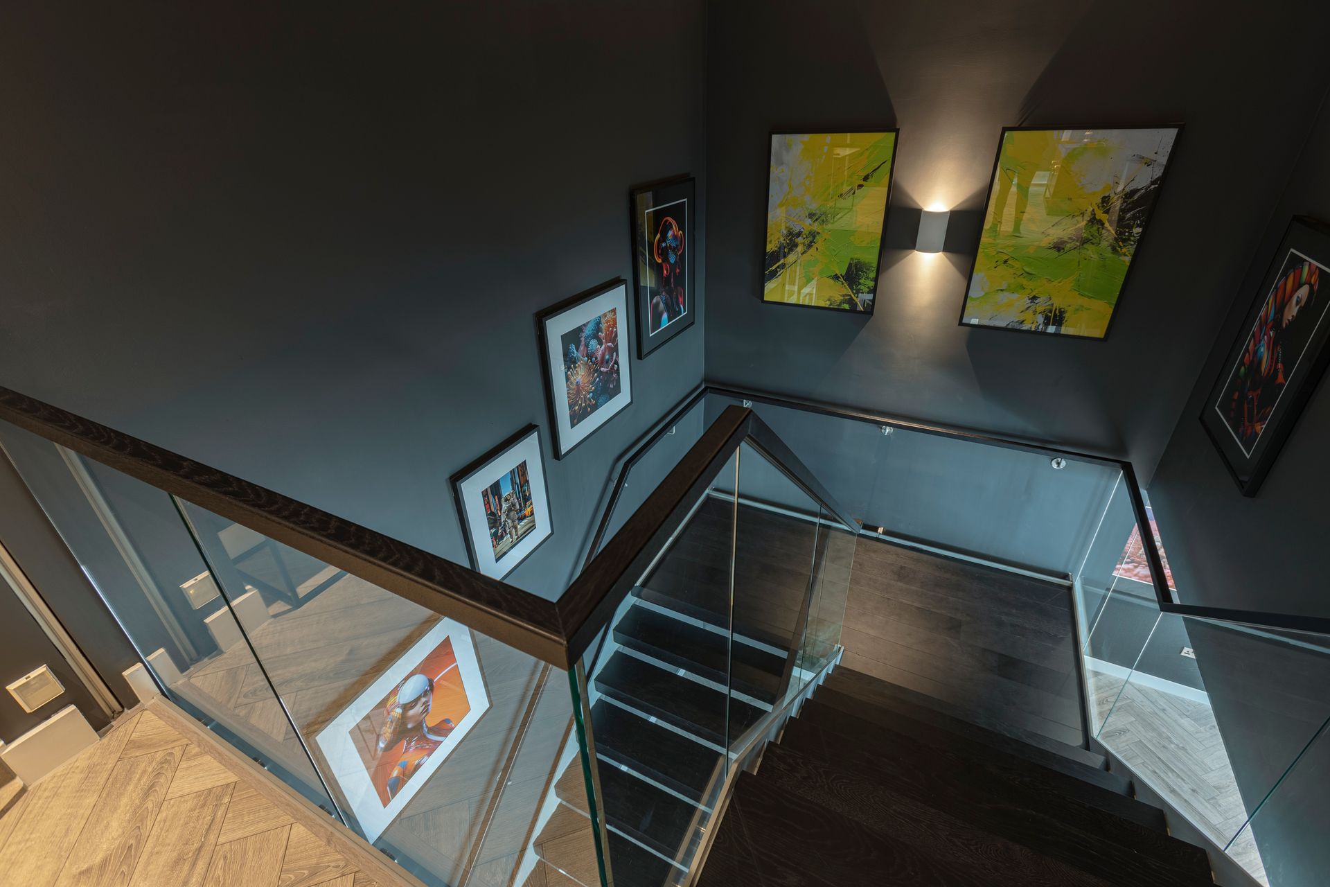 Stairwell with dark gray walls, artwork, and wooden steps. Glass railing.