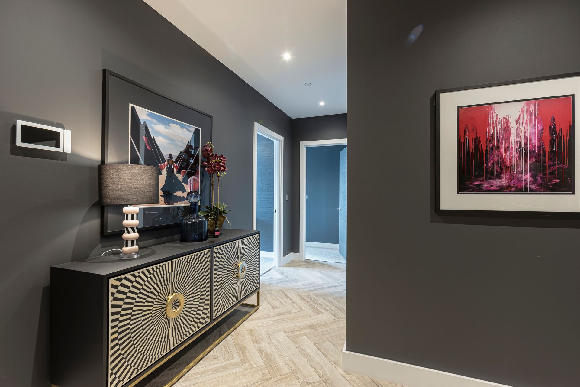 Dark gray hallway with patterned cabinet, artwork, and light wood flooring.