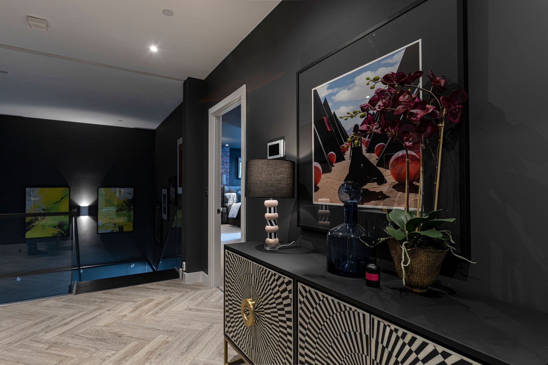 Dark hallway with black walls, a patterned cabinet, artwork, and an open doorway.