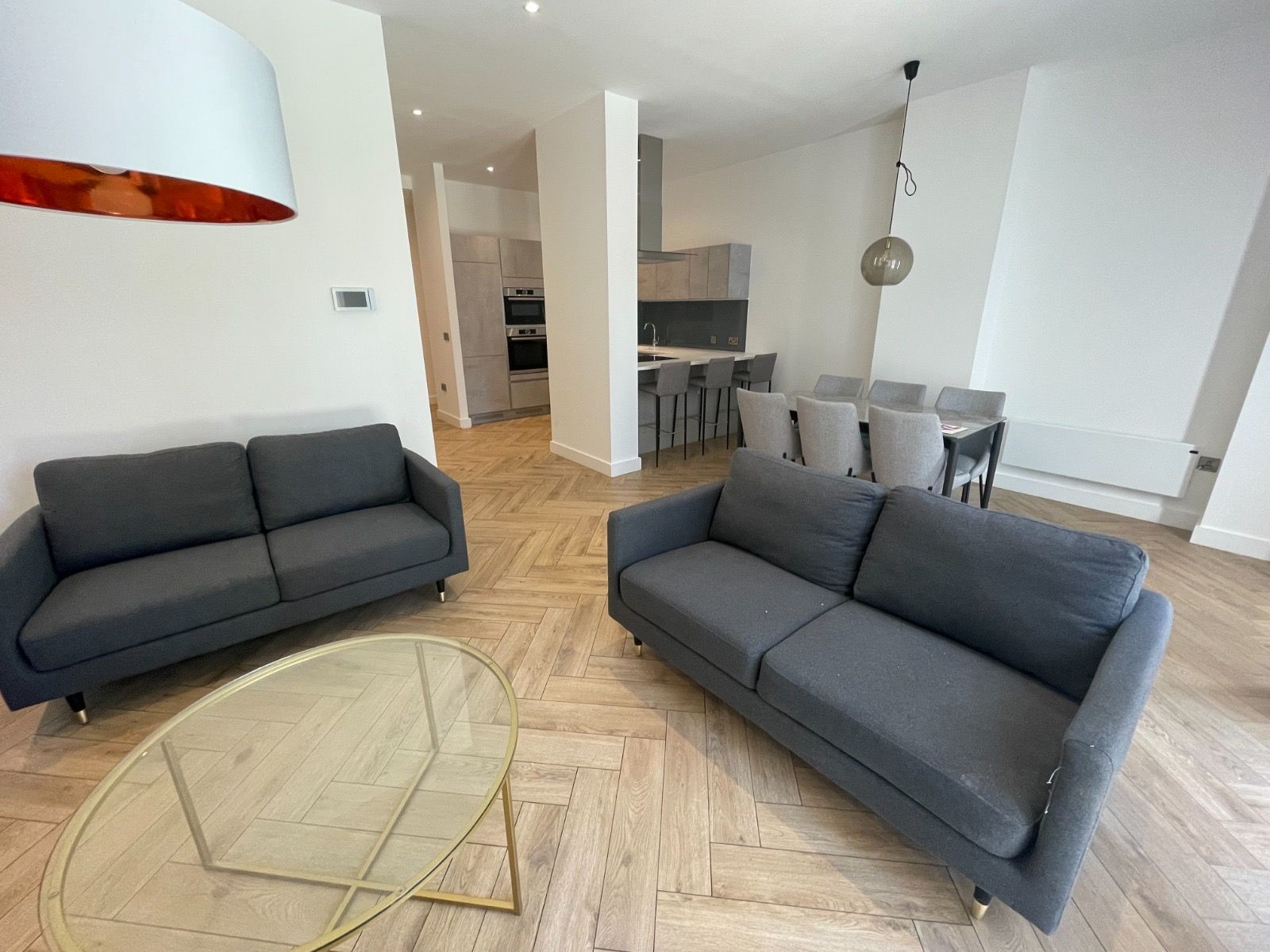 Modern living room with gray sofas, a glass coffee table, and an open kitchen.
