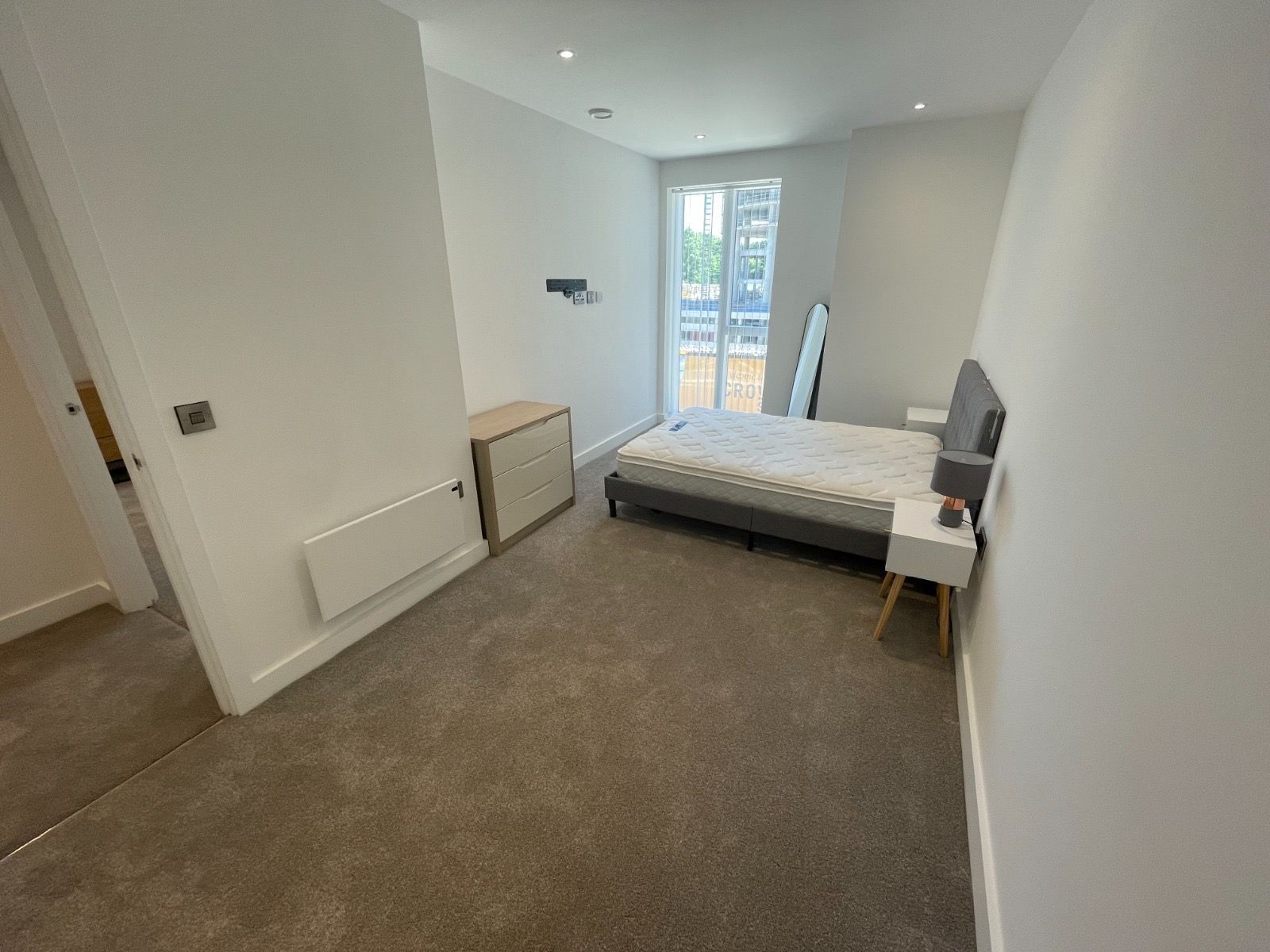 Bedroom with a bed, dresser, nightstand, and window. Gray carpet and white walls.
