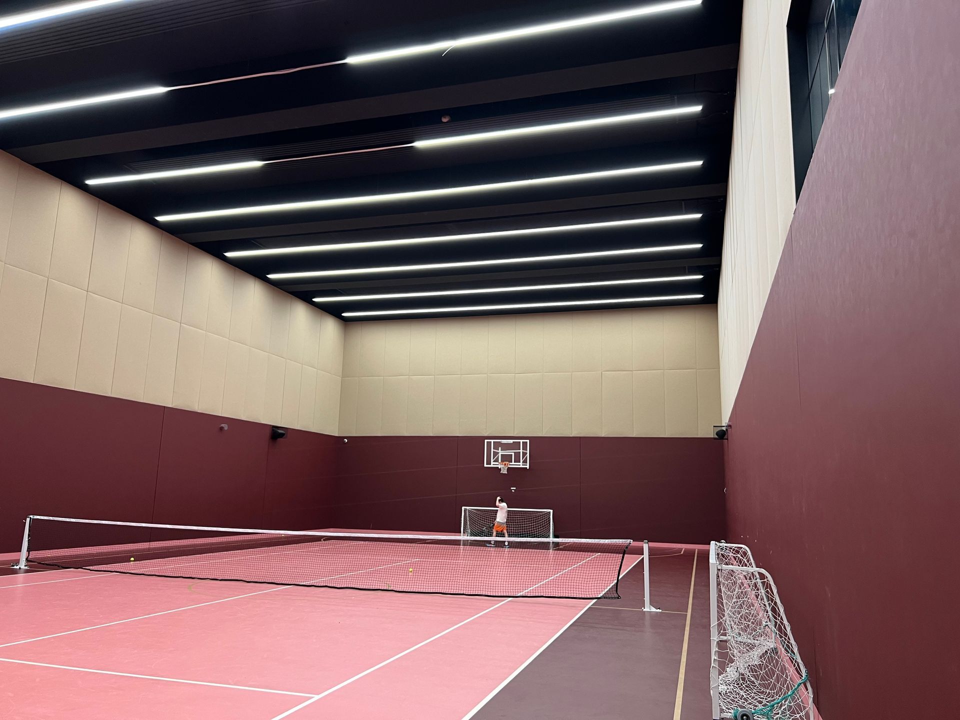 Indoor sports court with red flooring, burgundy walls, and basketball hoop.