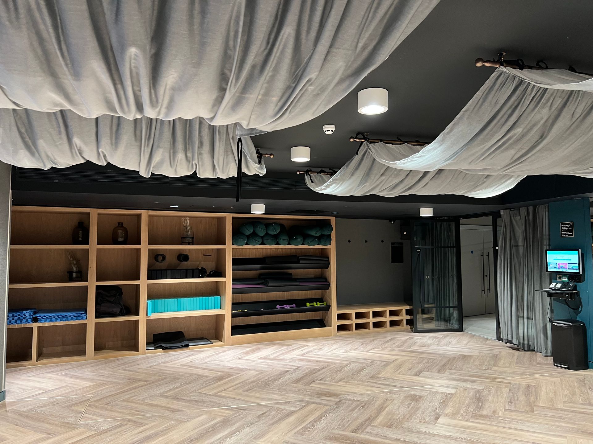 Yoga studio interior with wooden shelves, yoga mats, and draped fabric on a dark ceiling.
