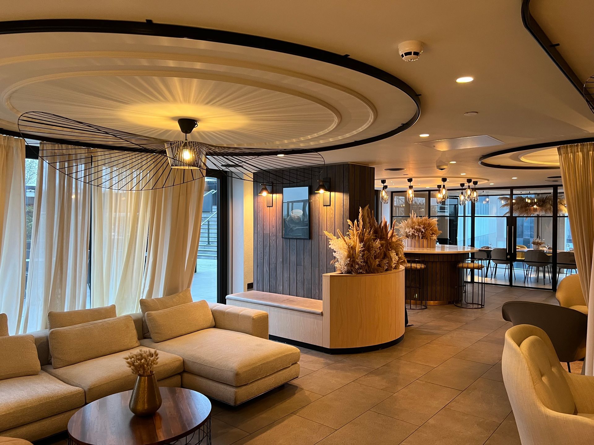 Cozy lounge with cream-colored sofas, circular ceiling design, and a bar area with tables and chairs.