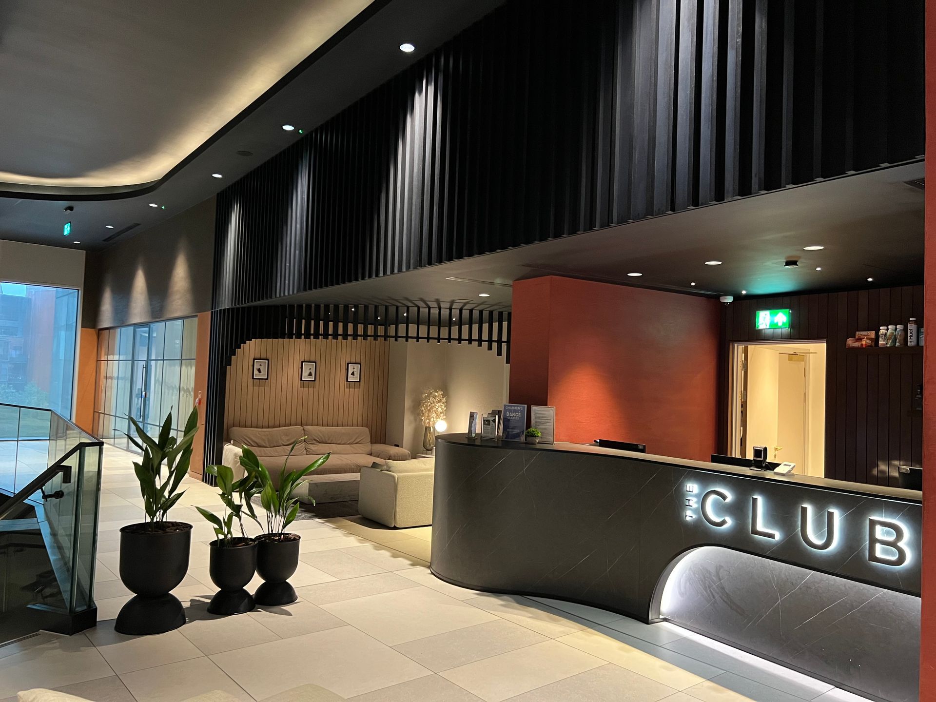 Modern lobby with reception desk, seating area, potted plants, and dark wall features.
