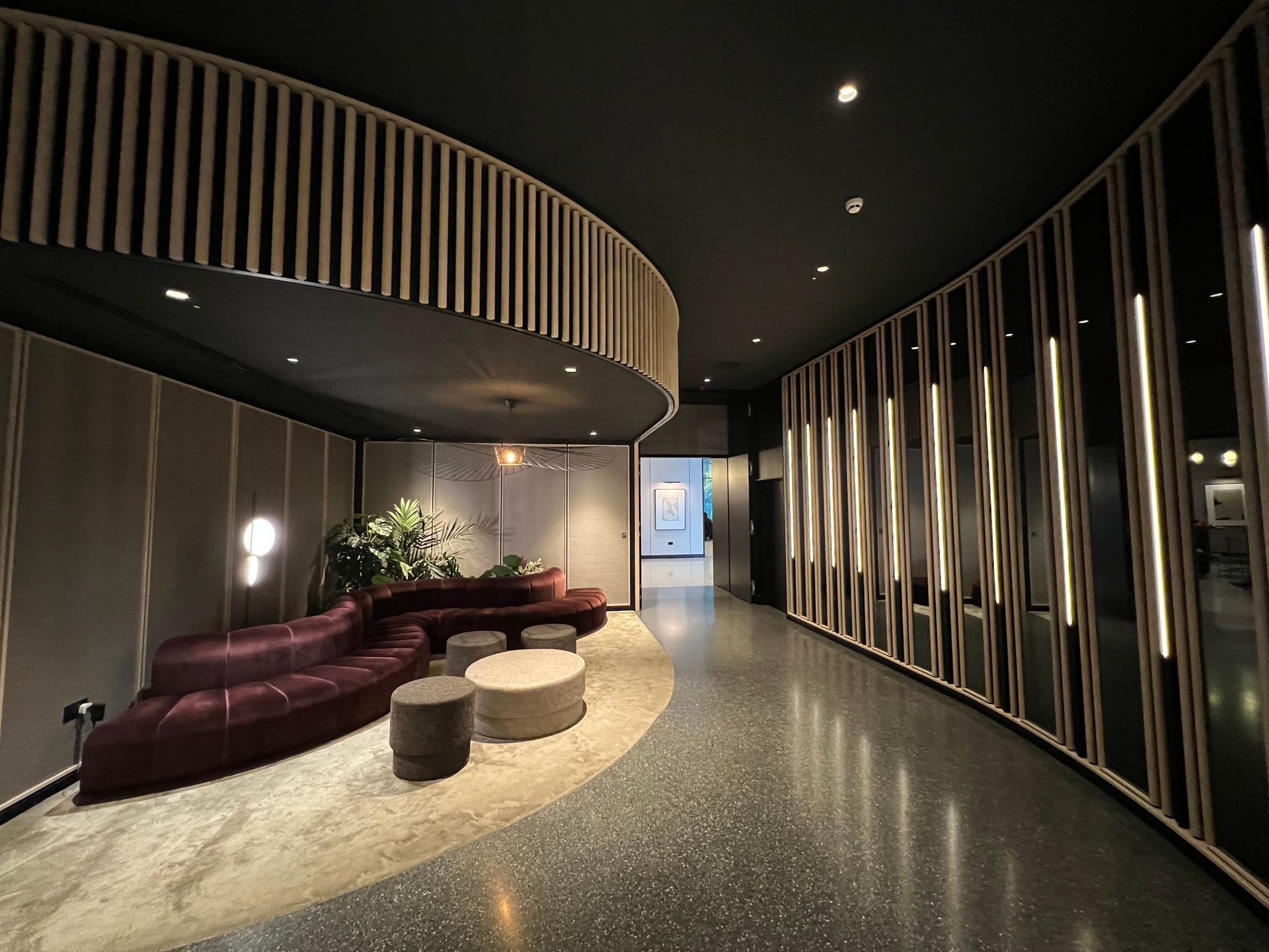 Modern hallway with curved walls, dark ceiling, and a seating area with a maroon sofa.