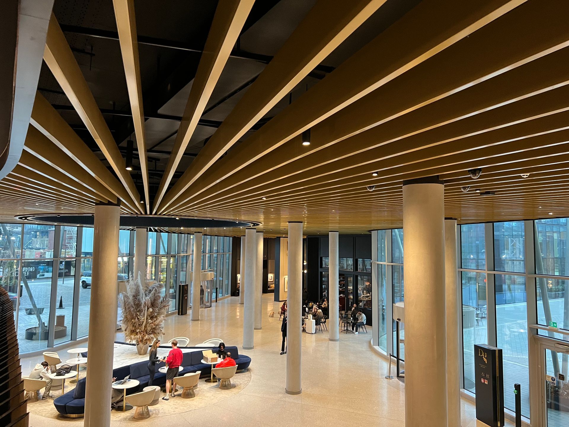 Modern interior with a golden ceiling, tall columns, and a glass wall with people seated at tables.