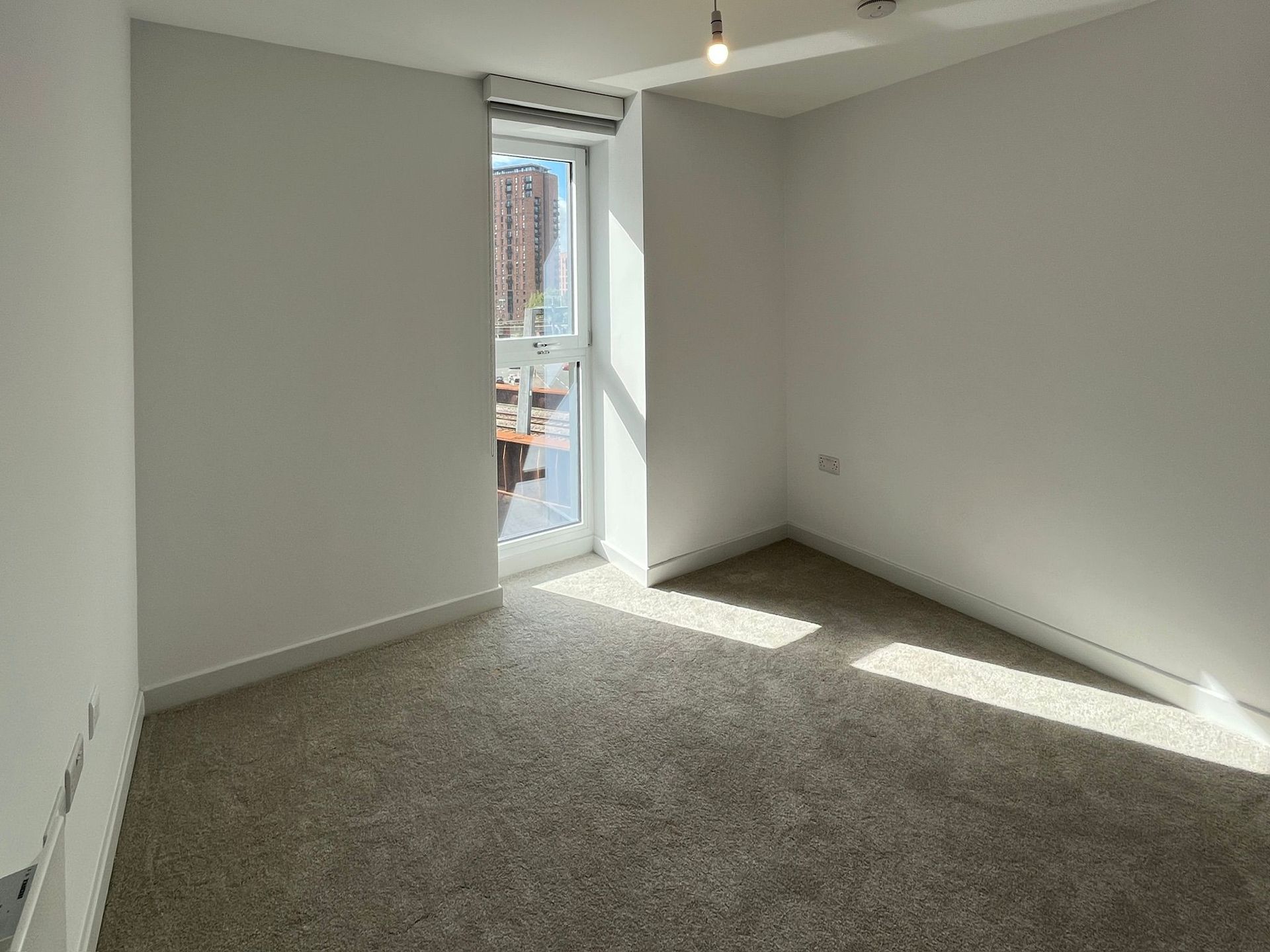 Empty room with beige carpet, white walls, and a glass door letting in sunlight.