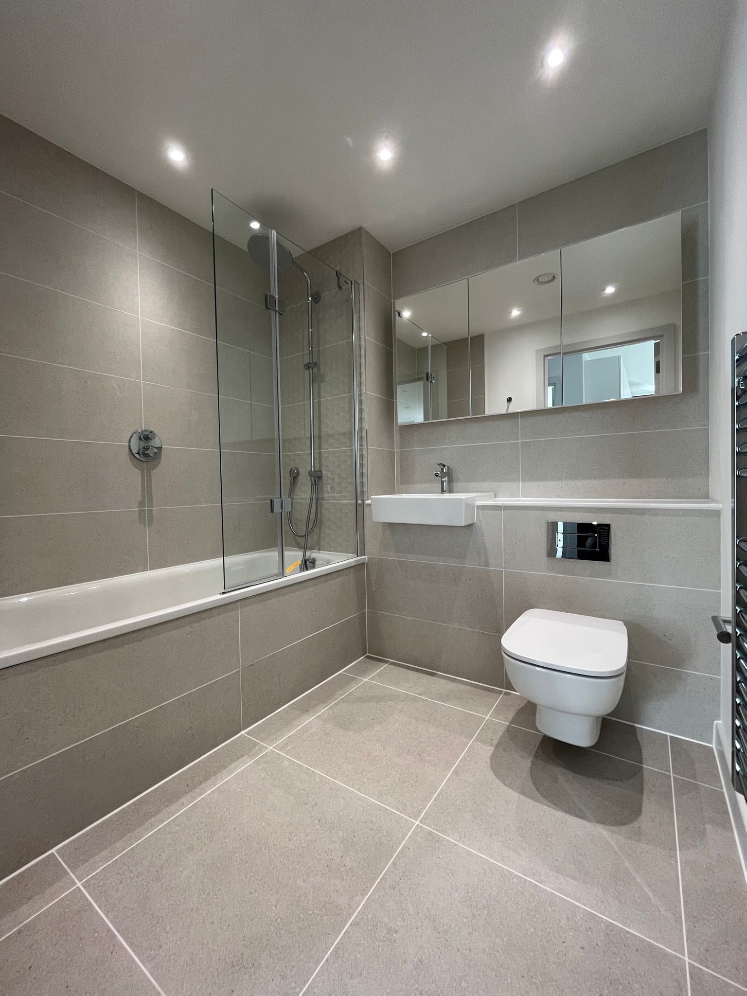 Modern bathroom with gray tiles, a bathtub, toilet, and sink.