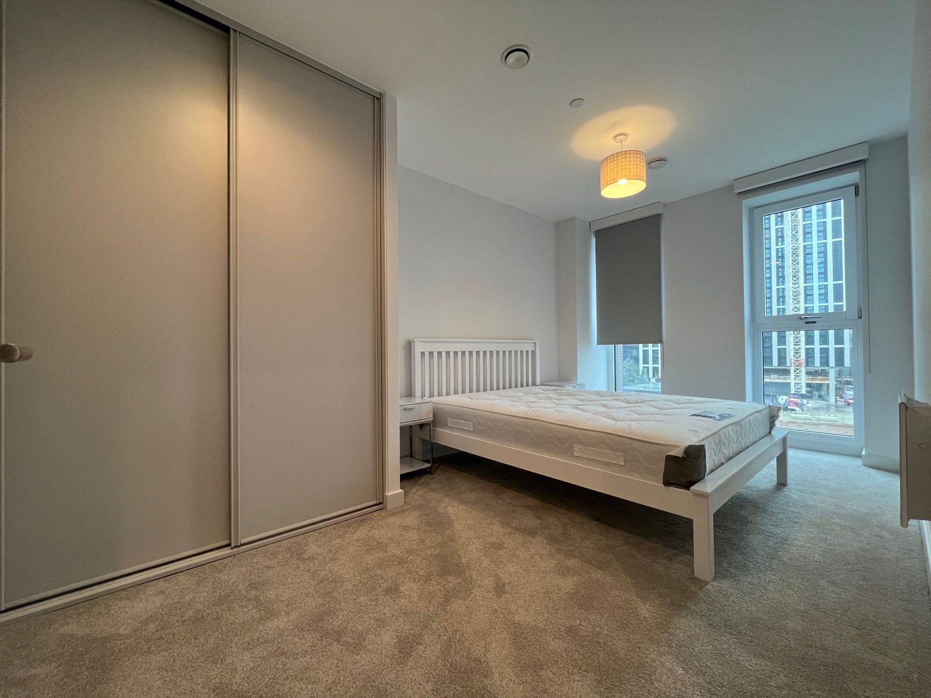 Bedroom with a white bed, large gray wardrobe, and a window with a city view.