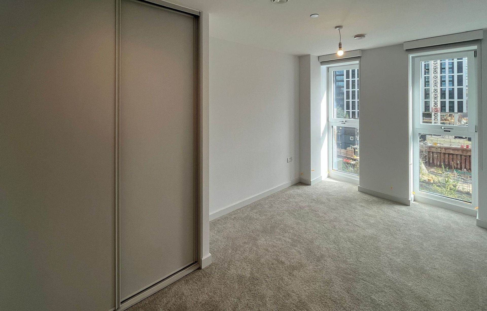 Empty bedroom with a built-in wardrobe, two windows, and light carpet.