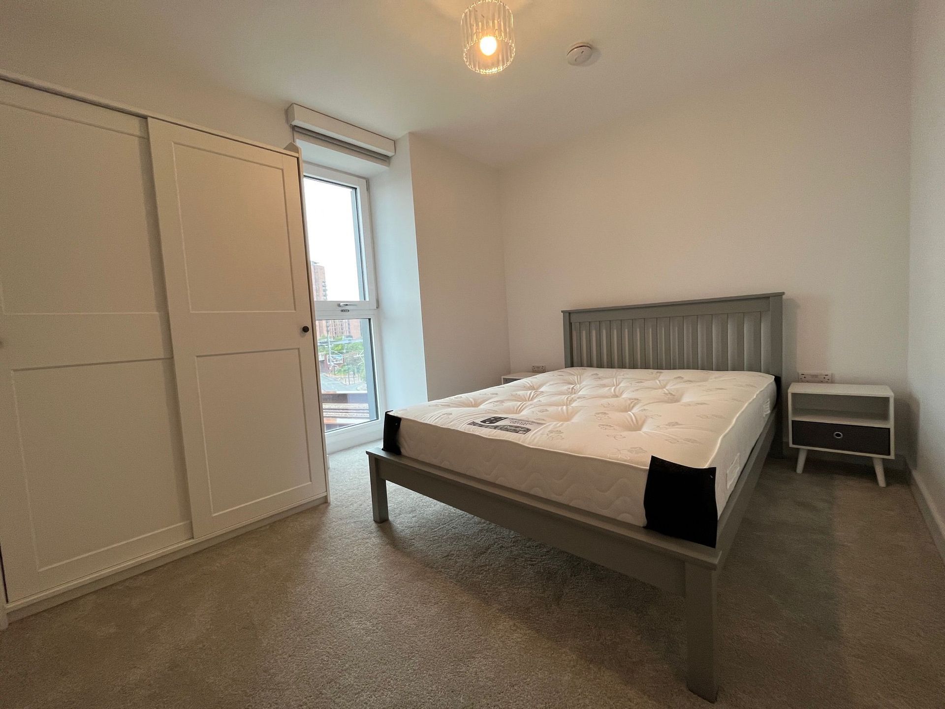 Bedroom with gray bed, white wardrobe, small nightstand, and window.