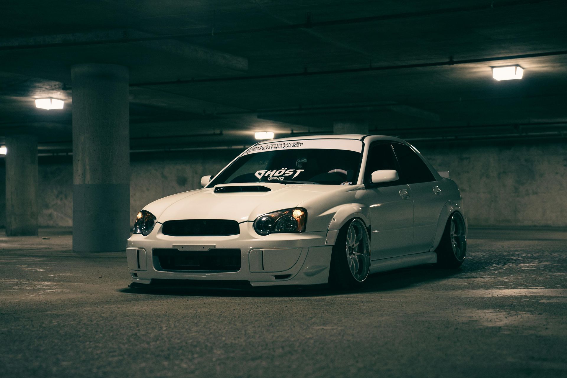 White Subaru WRX in a dark parking garage, modified with custom body kit and lowered suspension.