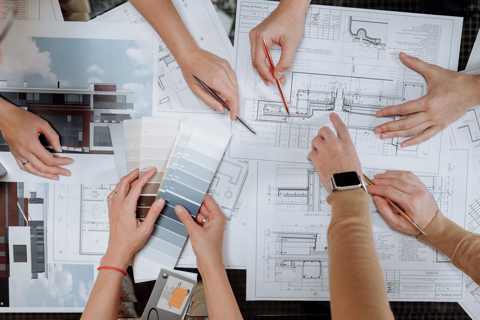 Hands around blueprints and color swatches, collaborating on a design project.