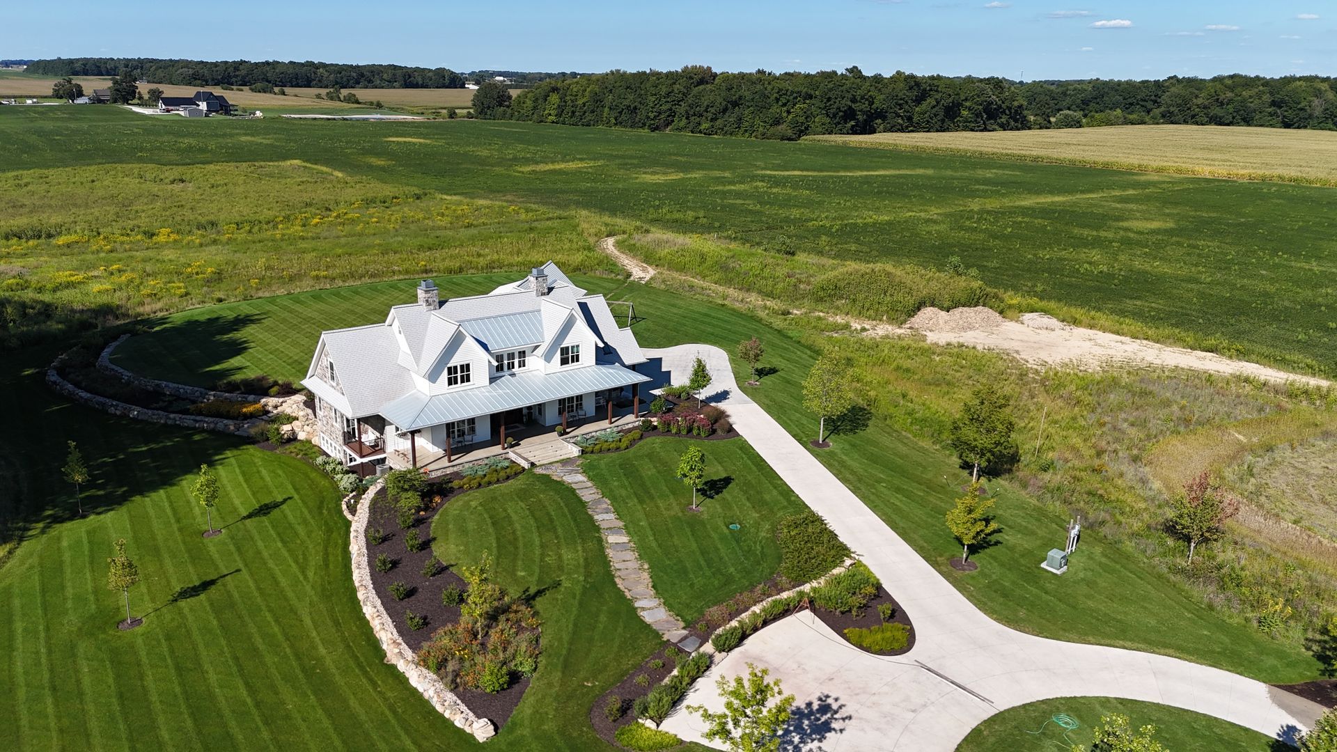 White farmhouse with a long driveway on a grassy hillside, surrounded by fields.