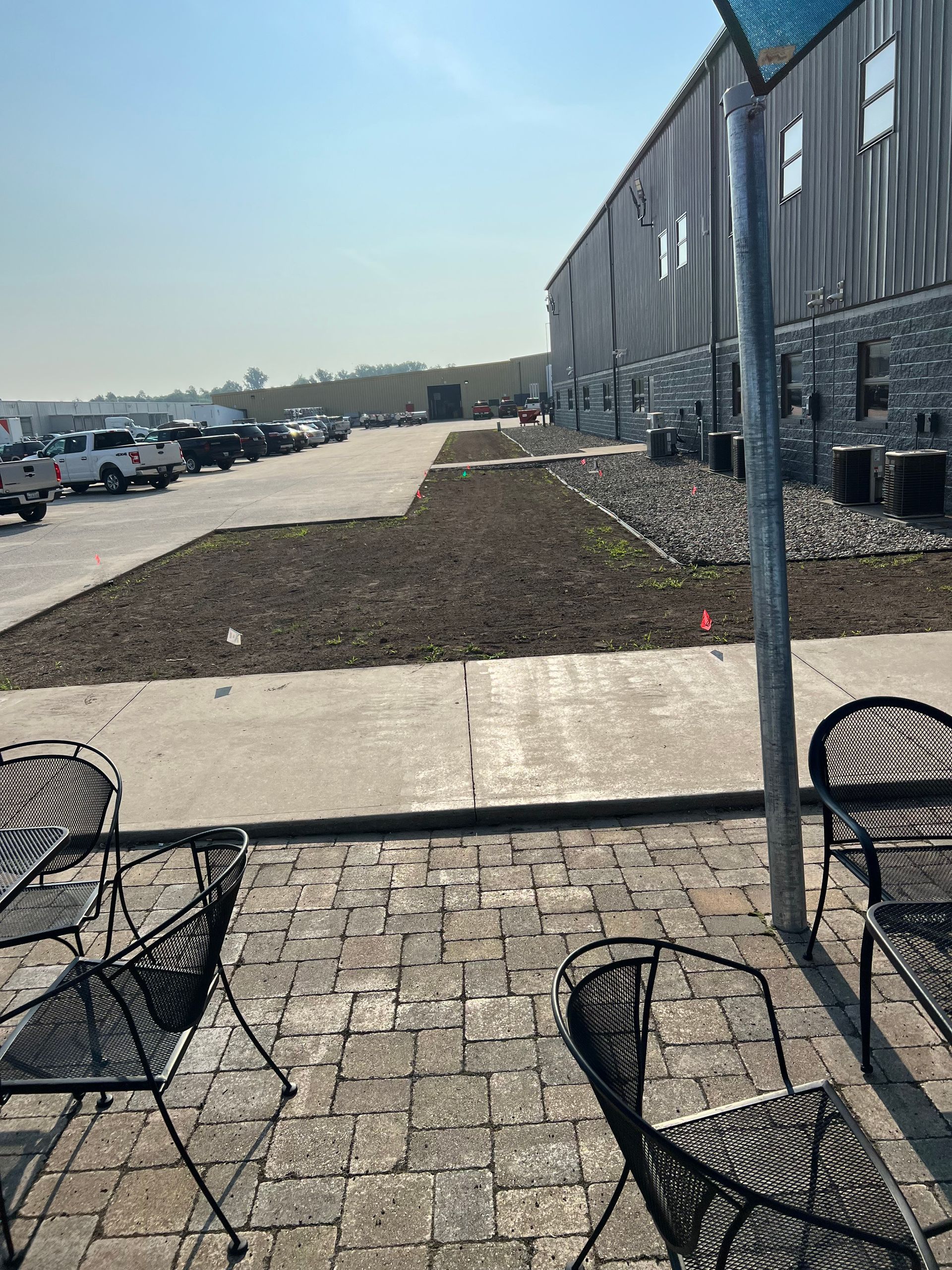 Outdoor patio with brick pavers, black metal chairs, and a building in the background. Parking lot visible.