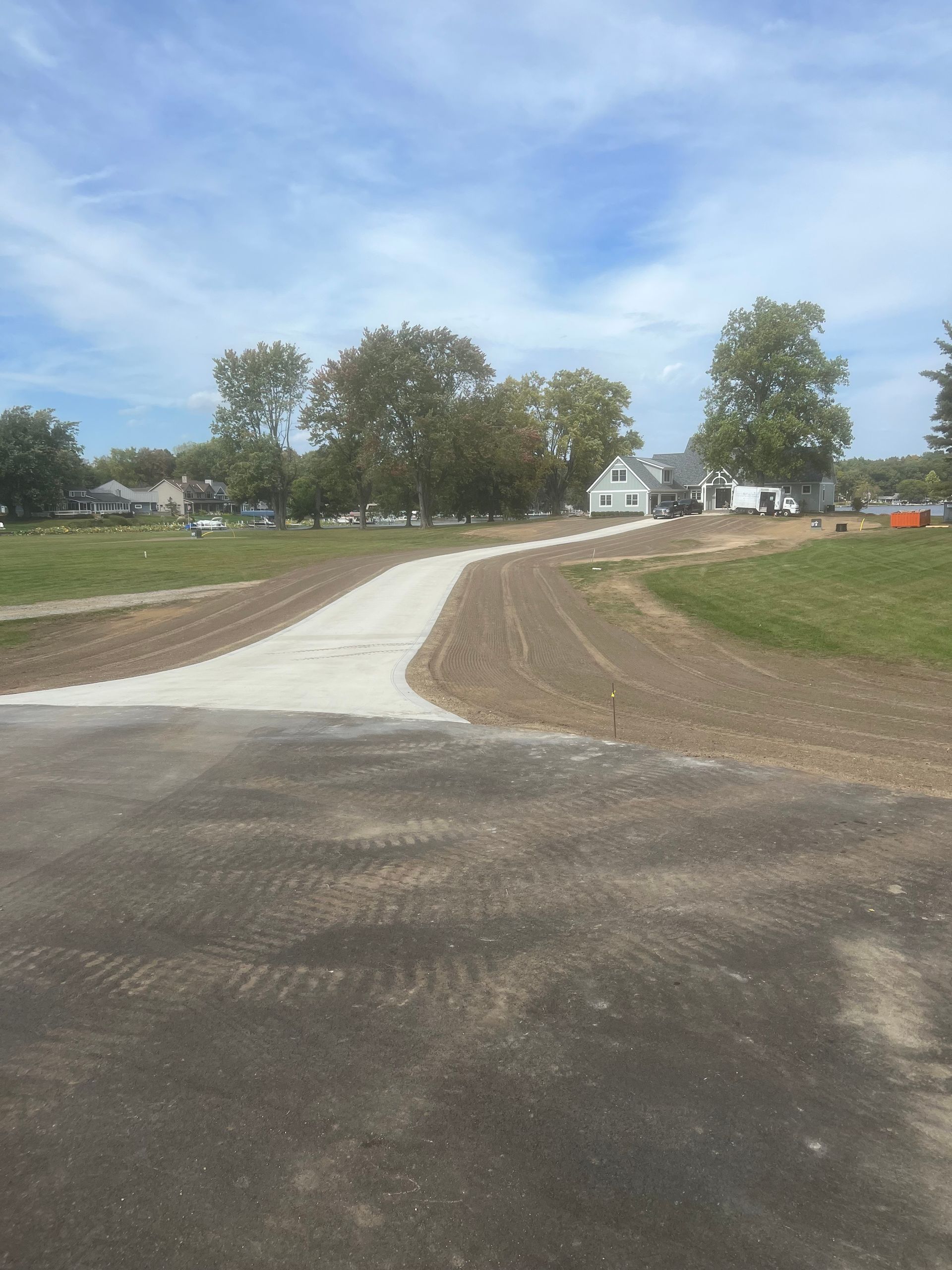 Asphalt road meets gravel pathway, leading toward houses under a blue sky.