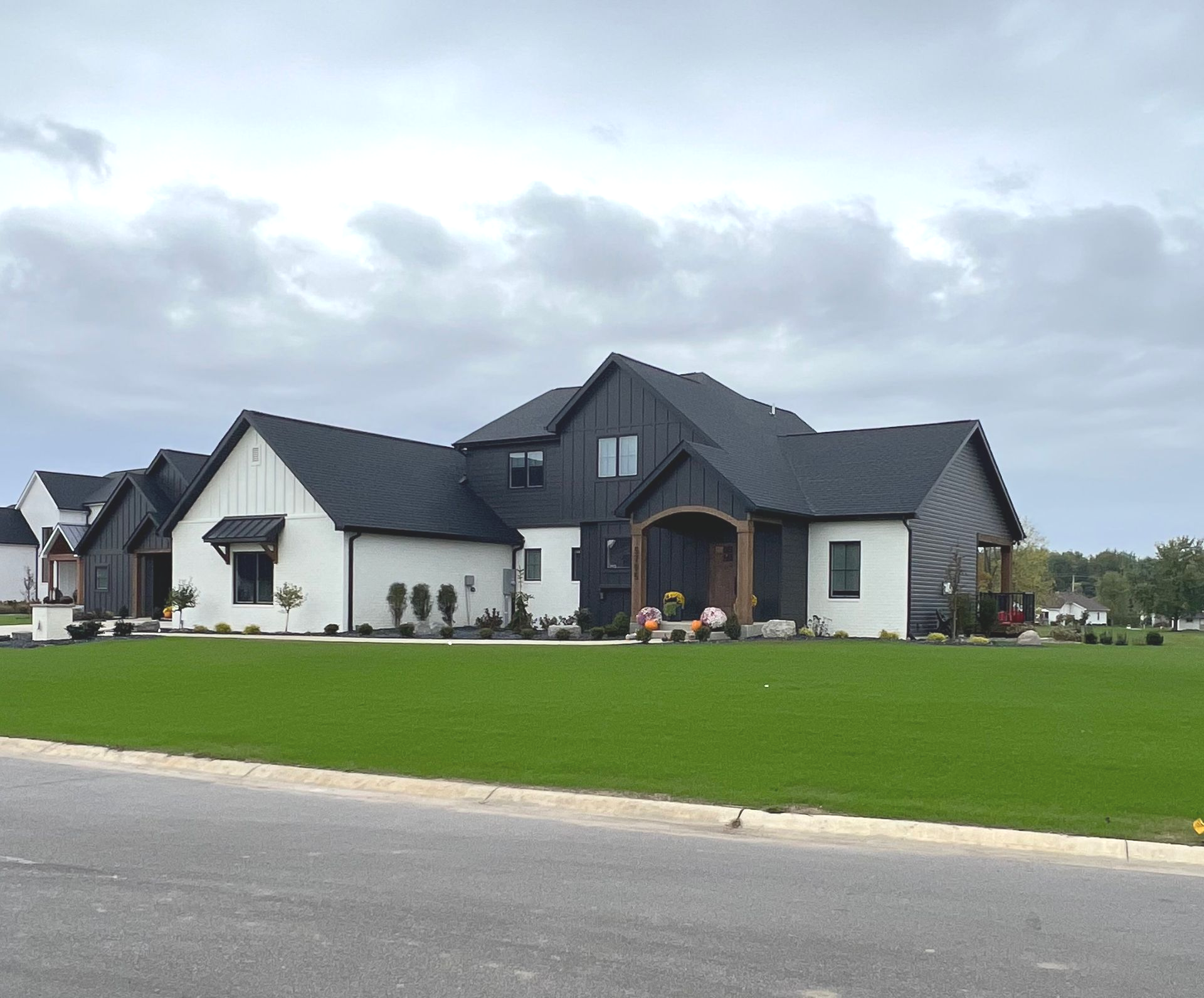 Modern farmhouse-style house with black roof and trim, white siding, and green lawn under a cloudy sky.