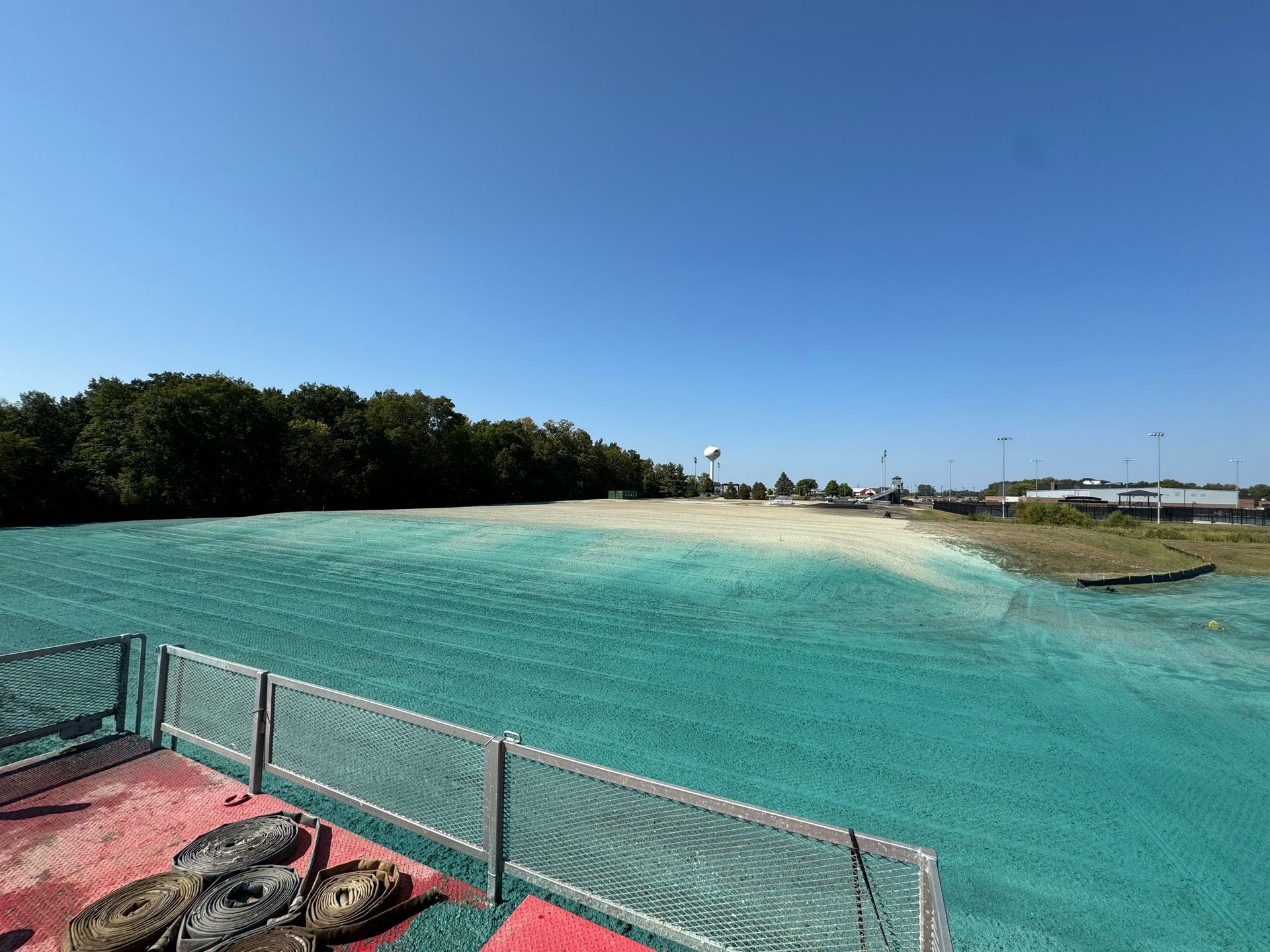 View of a turquoise wave pool under a clear blue sky, with trees and buildings in the background.
