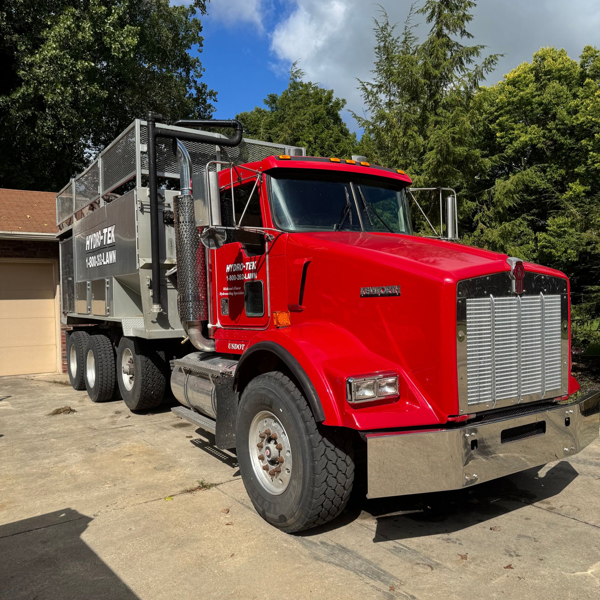 Red Kenworth truck with a silver debris container parked on a paved driveway.