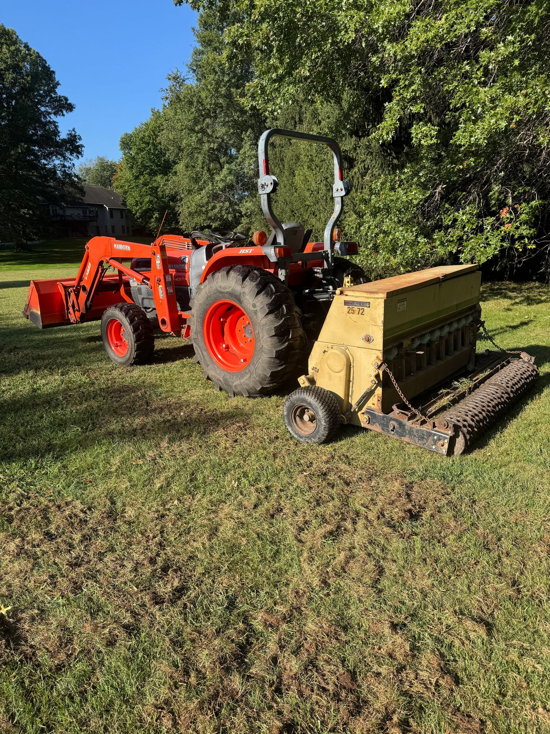 Orange tractor with attached seeder on a grassy lawn.