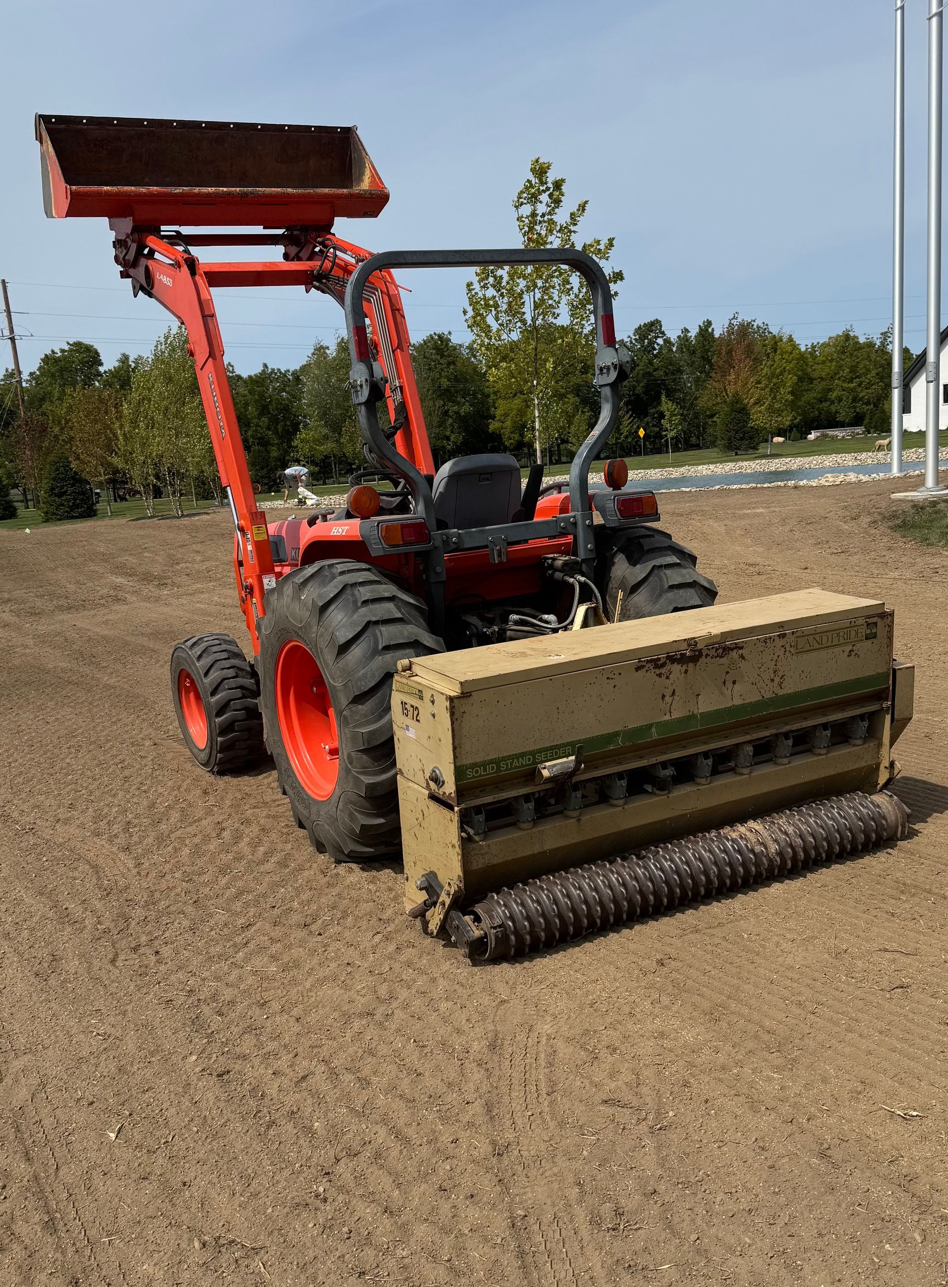 Orange tractor with seeder on a field of loose dirt.