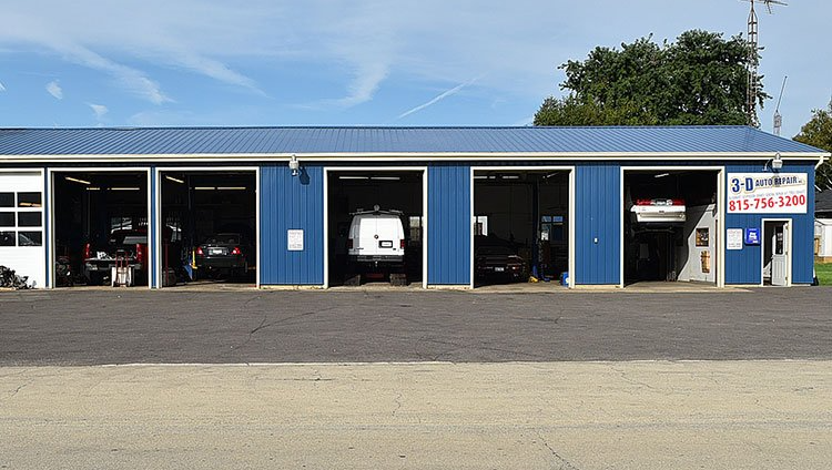 Blue auto repair shop with open bays, vehicles inside, and a sign.