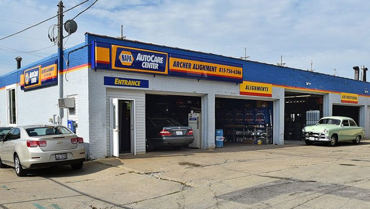 NAPA Auto Care shop with open garage bays, cars, blue and yellow signage, and an outdoor setting.