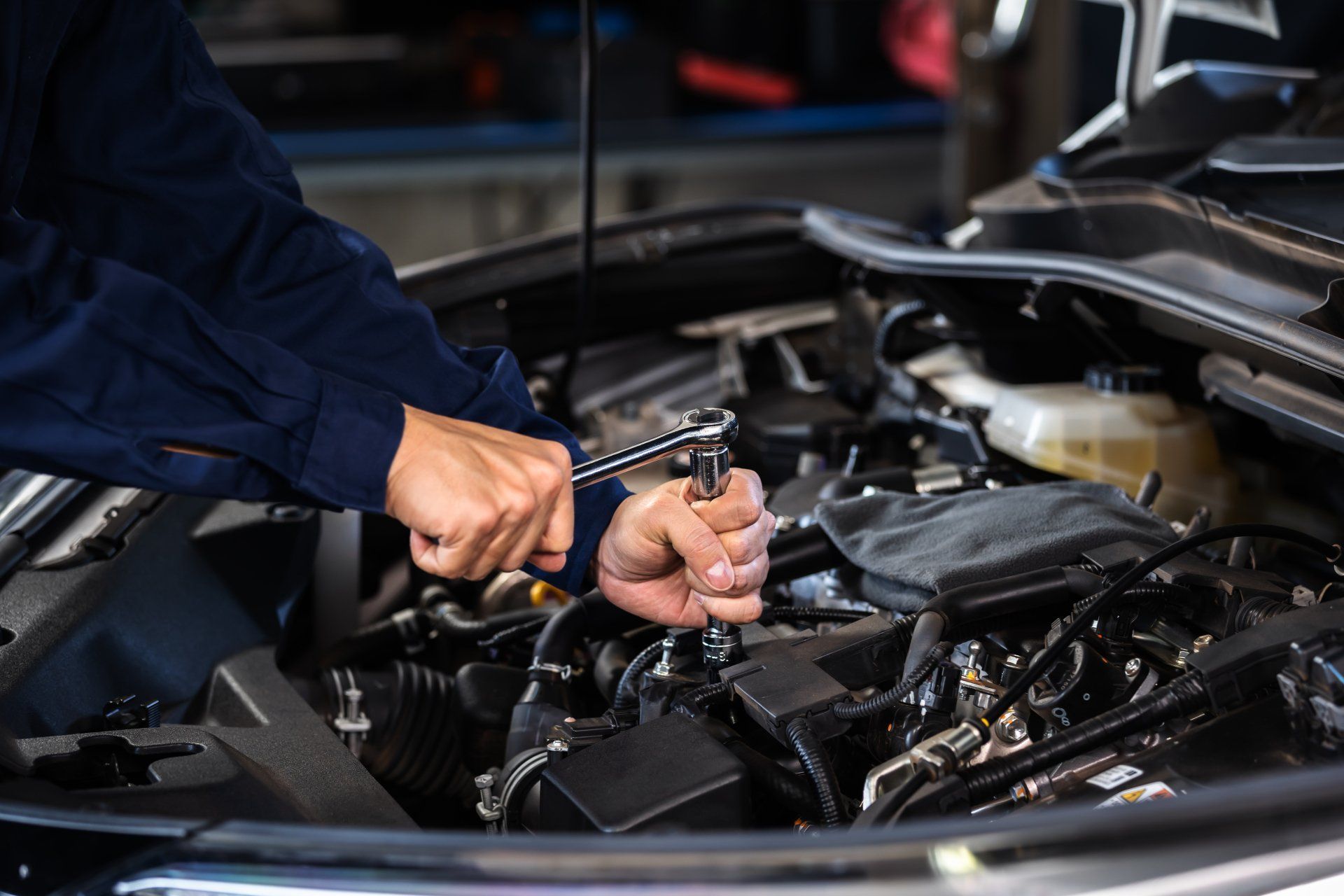 Mechanic working on a car engine with a wrench, in a garage setting.