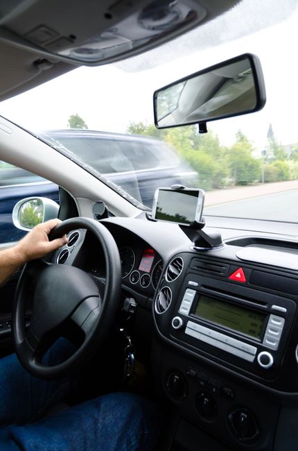 Vista del conductor dentro de un automóvil, con las manos en el volante y un teléfono montado en el tablero.