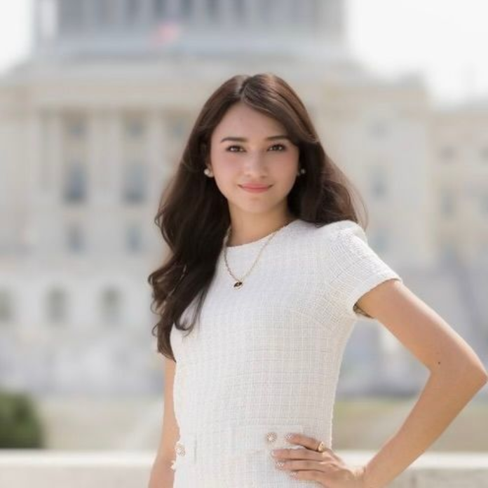 Woman in a white dress posing outdoors with a blurred building in the background