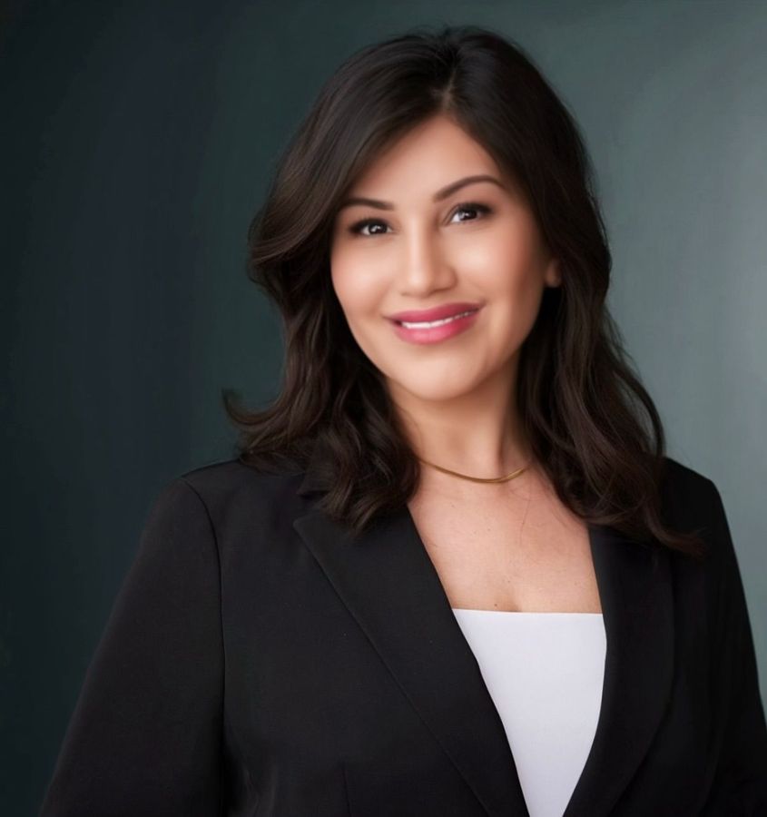 Portrait of a smiling woman with long dark hair in a navy blazer, indoors with a blurred background