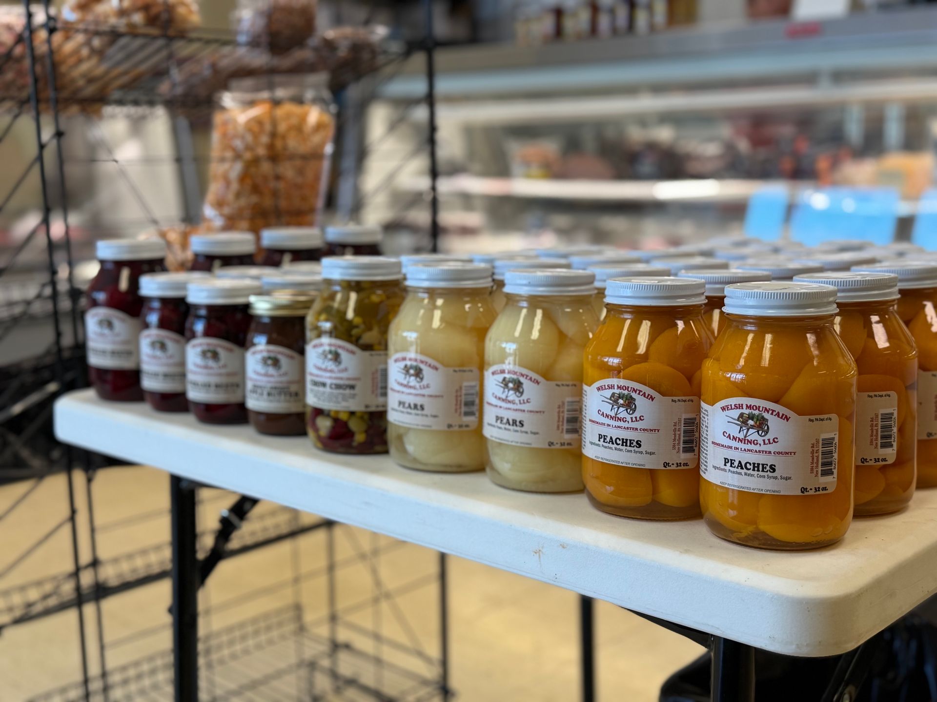 Jars of preserves displayed on a market table, with shelves and goods in the background