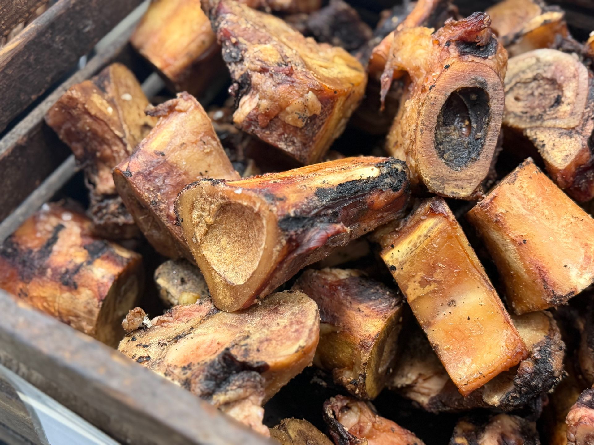 Pile of chopped firewood logs with bark and cut ends, stacked in a tray or bin.