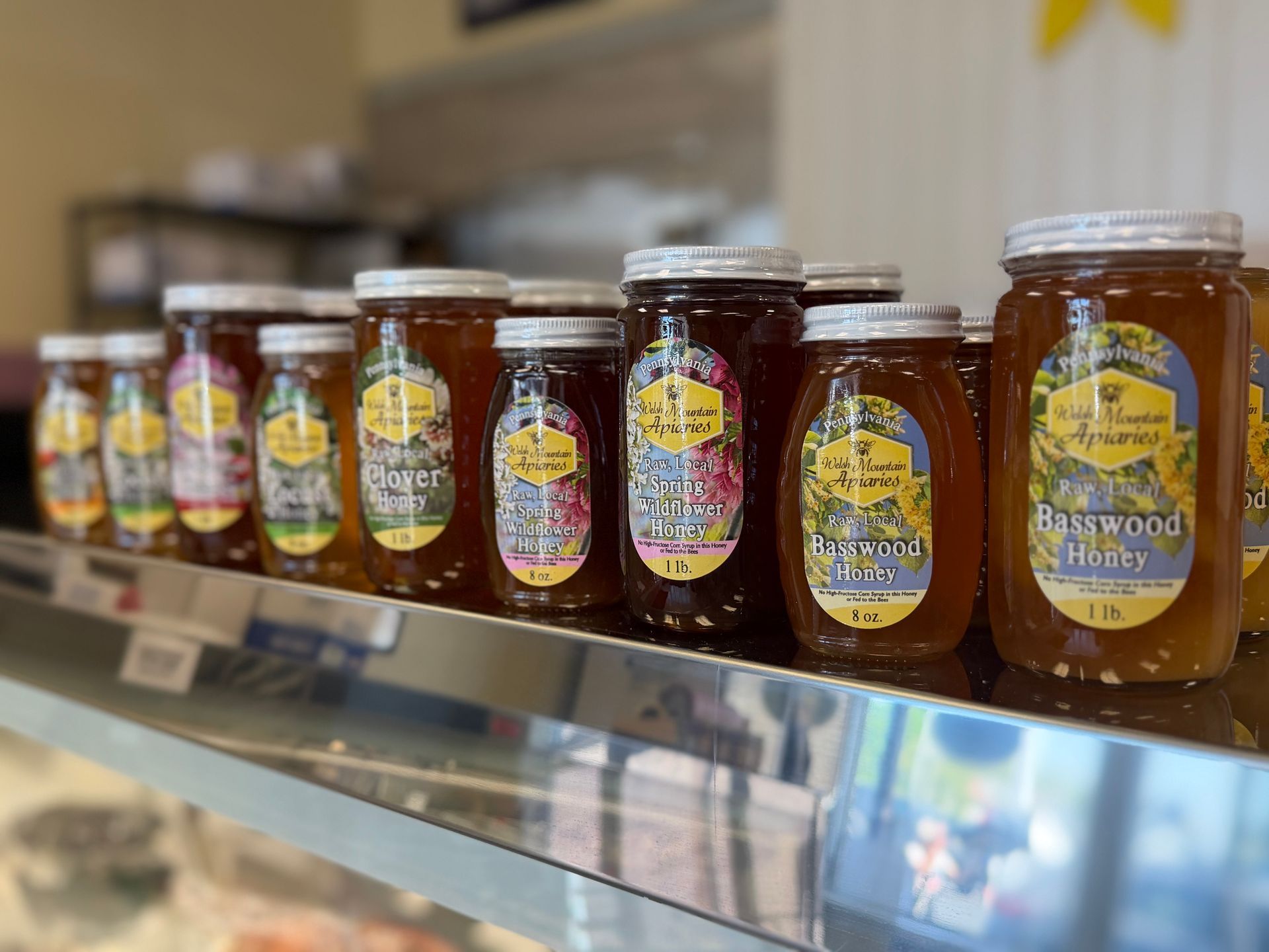 Rows of honey jars on a store shelf, with amber and dark labels in a grocery aisle.