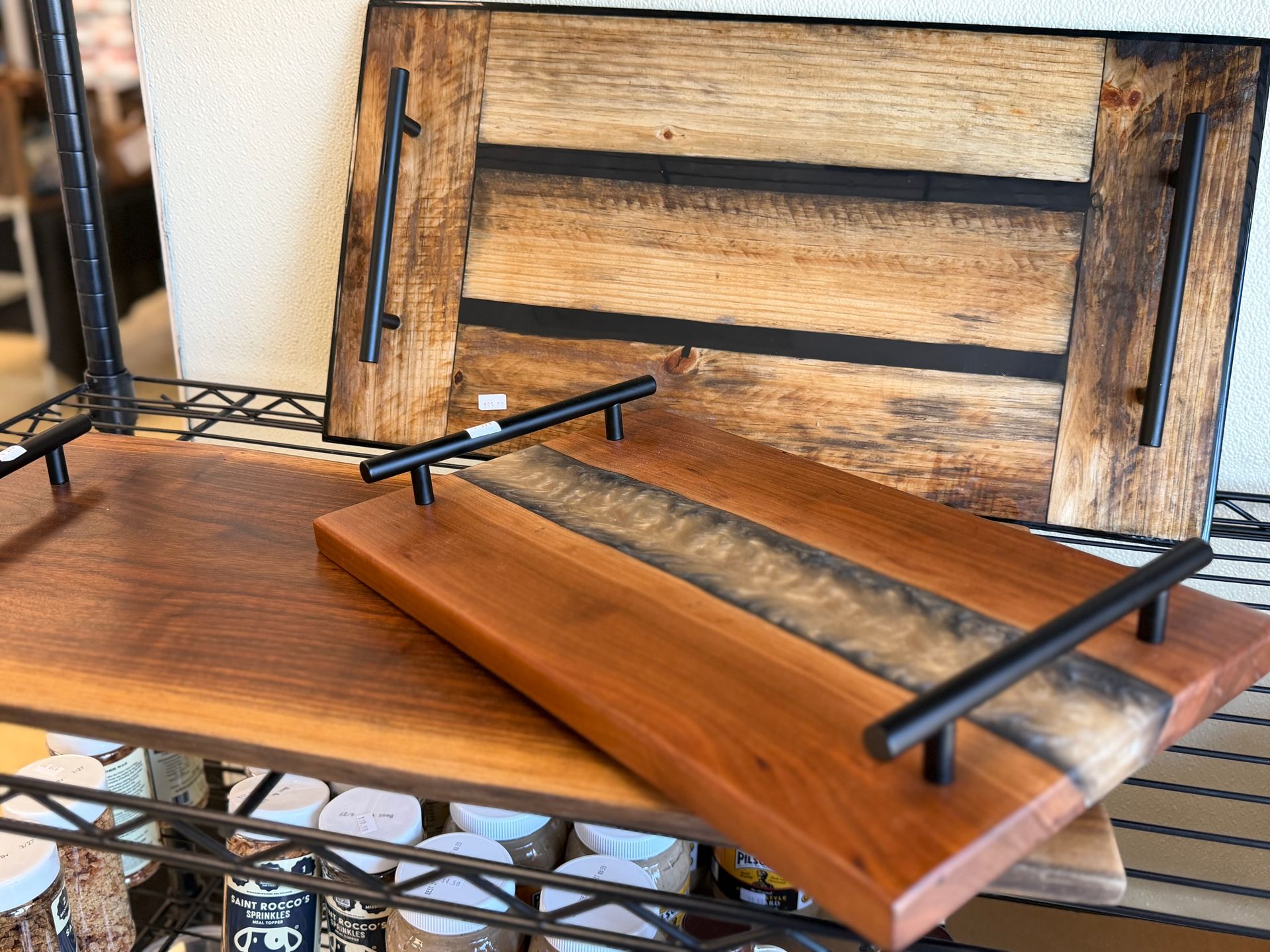 Wooden trays with black handles on a metal shelf, one open against a rustic wood backdrop